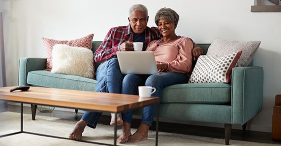 two seniors sitting on a couch looking at a laptop