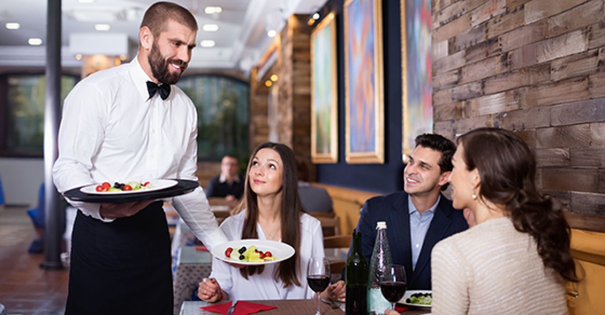 Waiter delivering plated food to couple sitting at a table